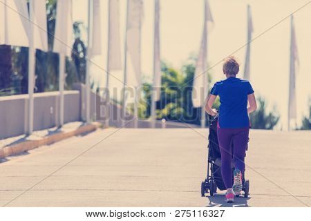 young healthy mother jogging while pushing a baby stroller at city park