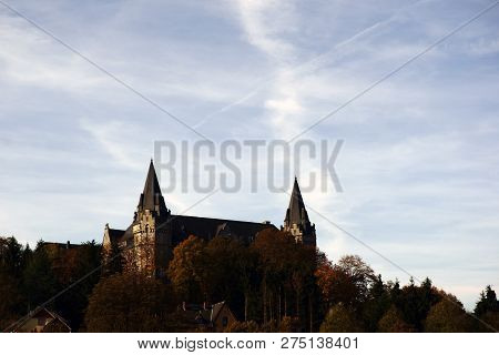 The Towers Of Abbey Sayn In Hadamar Above The Treetops Of Trees On A Mountain.