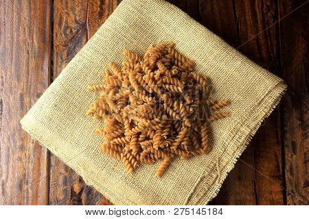 Top View Of The Whole Mass Of Fusilli, On Fabric, Rustic Towel With Wooden Spoon, On A Wooden Backgr