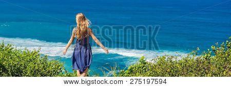 Young Woman Tourist On A Cliff Above The Beach. Empty Paradise Beach, Blue Sea Waves In Bali Island,