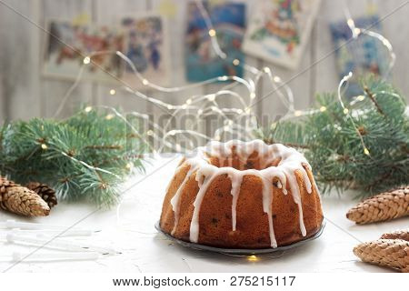 Pie With Raisins And Icing From Powdered Sugar On The Background Of Fir Branches And Garlands. Rusti