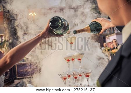 Man And Woman Holding Bottles Of Champagne In Their Hands Pouring Drink By The Glass