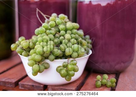 Front View Of Bunches Of Yellow-green Ripe Grapes From An Organic Garden. Big Wine Bottles Aback. Se