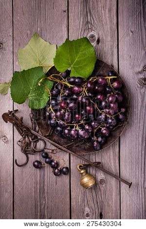 Still Life With Black Grapes In An Old Steelyard On Rough Wooden Table