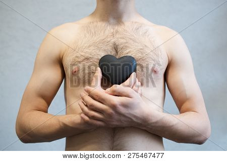 Portrait Of Black Heart In Man Hands, On Body Torso Background. Valentines Day Concept.