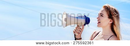 Girl Of Model Appearance Speaks Into A Loudspeaker Against A Blue Sky