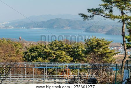 Landscape Of Reservoir On Hazy Overcast Day With Mountains, City Buildings And  In Background And Wa