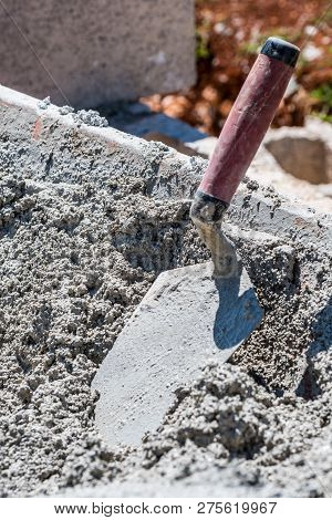 Mixed wet cement in wheelbarrow with red handle trowel dipped in. Outdoor construction work site.