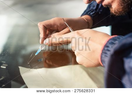 Close-up Of A Professional Windshield Repairman Fills A Crack In The Glass With A Special Polymer Th