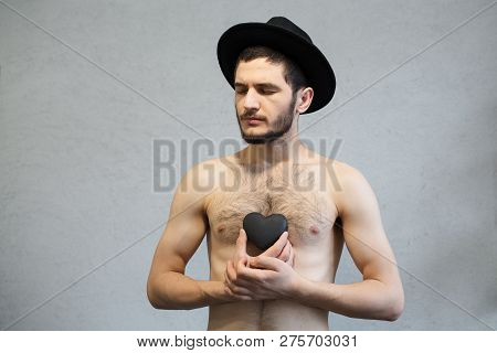 Young Naked Man, With Black Stone Heart In Hands. With A Black Hat On His Head.