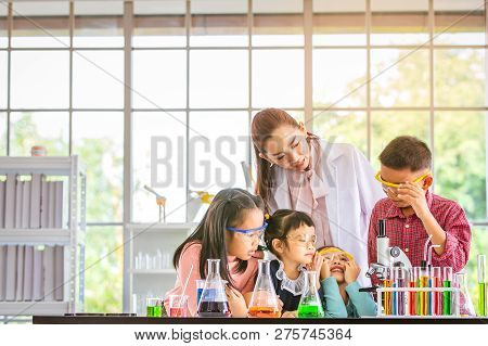 Science Teacher Teach Asian Students In Laboratory Room, Boy  Look Through Microscope, Colorful Test