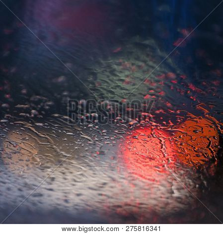 Abstract Pattern Of Colorful Lights And Rain Drops During Downpour On Winshield Of Car After Dark