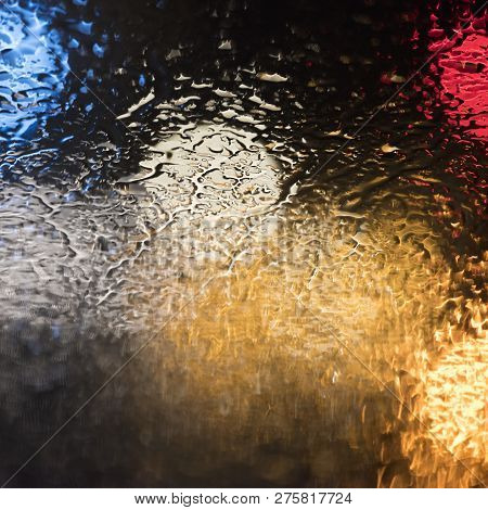 Abstract Pattern Of Colorful Lights And Rain Drops During Downpour On Winshield Of Car After Dark