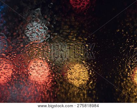 Abstract Pattern Of Colorful Lights And Rain Drops During Downpour On Winshield Of Car After Dark
