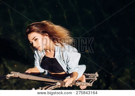 Ambition Is Her Only Stimulus. Sensual Woman Hang On Rope Over Water Surface. Sexy Woman Climbing Up