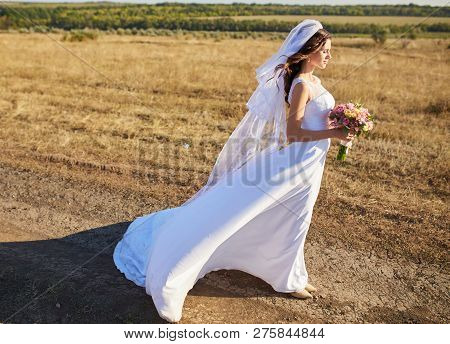 Beautiful Smiling Bride Wearing A Natural Flower Wreath And Standing In The Golden Summer Fields Wit