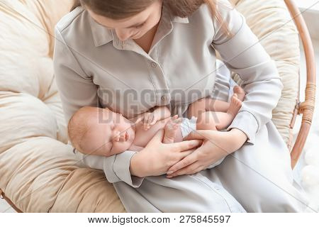 Young Mother With Her Newborn Baby In Papasan Chair At Home