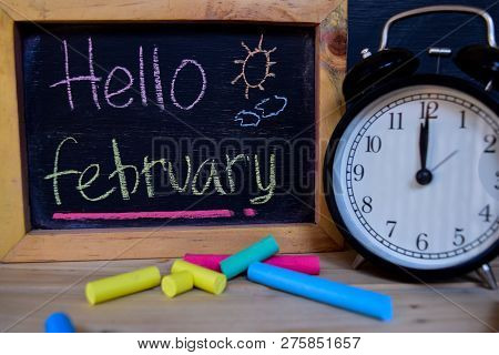 Hello February. Back To School Concept. Alarm Clock On Wooden With Blackboard On Background