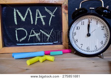 May Day. Back To School Concept. Alarm Clock On Wooden With Blackboard On Background
