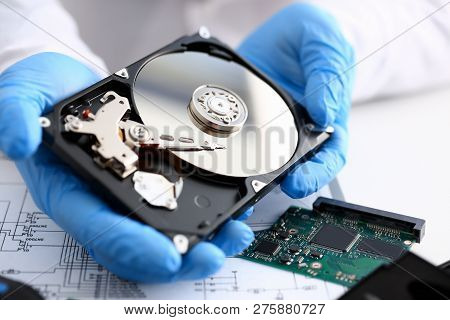 Male Repairman Wearing Blue Gloves Holding Hard Drive From Computer Or Laptop In Hands. Performs Fau