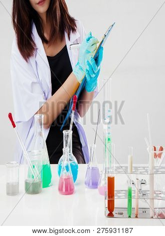 The Chemist In Protective Eyeglasses Working By Test Tube With Reagent In Lab,she Is Writing The Res