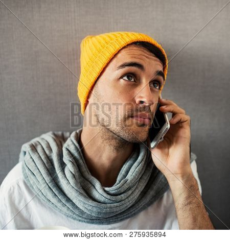 Close-up Portrait Of Young Handsome Man Speaking On Telehone, Wearing Orange Hat And Gray Scarf On G
