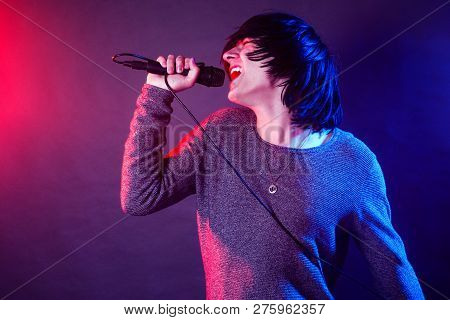 The Young Guy Vocalist Is Screaming In Microphone On Stage On Concert Illuminated With Red And Blue 