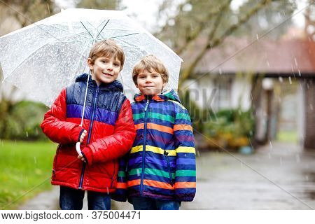 Two Little Kid Boys On Way To School Walking During Sleet, Rain And Snow With Umbrella On Cold Day. 