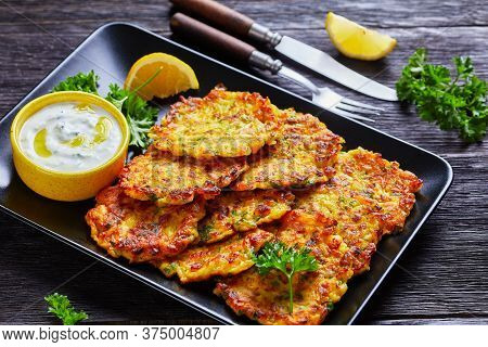 Greek Tzatziki Sauce And Crispy Onion Latkes Served On A Black Plate With Lemon And Fresh Parsley On