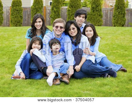 Большое семейство семи сидеть вместе на лужайке, одетые в синие цвета