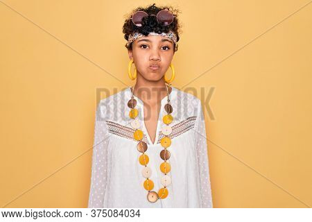 Young beautiful african american afro hippie woman wearing sunglasses and accessories puffing cheeks with funny face. Mouth inflated with air, crazy expression.