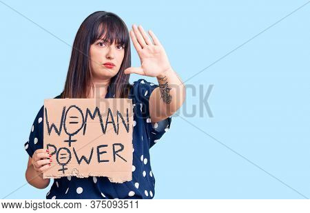Young plus size woman holding woman power banner with open hand doing stop sign with serious and confident expression, defense gesture 