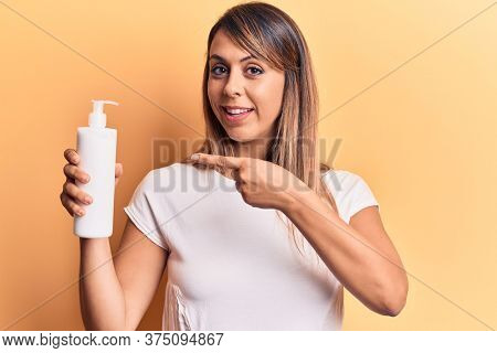Young beautiful woman holding bottle of cream lotion smiling happy pointing with hand and finger 