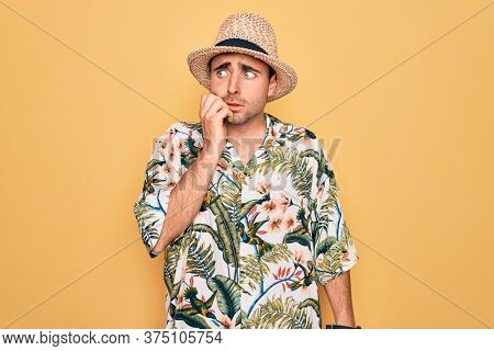 Young handsome man with blue eyes on vacation wearing summer florar shirt and hat looking stressed and nervous with hands on mouth biting nails. Anxiety problem.