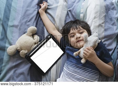 Kid Laying In Bed Playing With Soft Toy And Looking At Cameara With Smiling Face, Child Boy Lying In