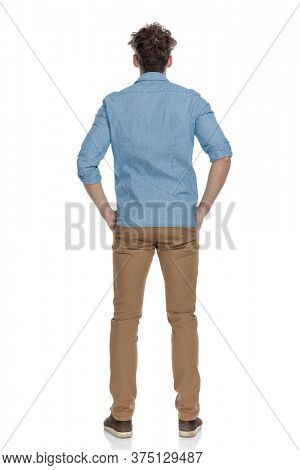 back view of young casual guy holding hands in pockets, standing isolated on white background, full body