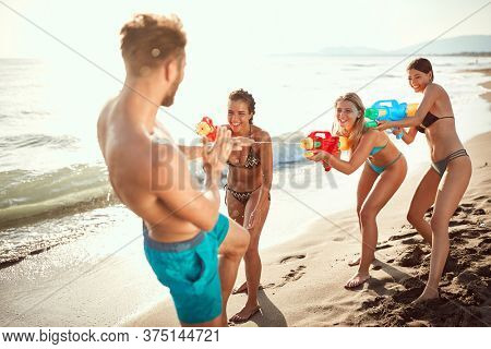 sexy women sprinkle beardy guy with water guns on sandy beach