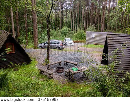 Holidays In Scottish Forest Nature. The Tourist Camp With Cottages And Modern Cars Parked Next To Th