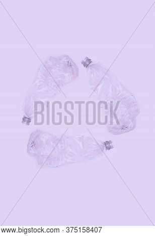 Three Crashed Plastic Bottles On Violet Background Form Resycling Sign. Plastic Utilisation Concept.