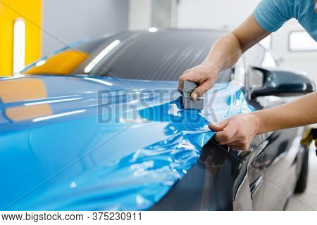 Car wrapping, mechanic with squeegee installs film