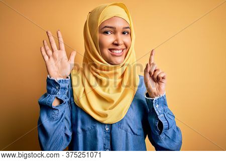 Young beautiful woman with curly hair wearing arab traditional hijab over yellow background showing and pointing up with fingers number six while smiling confident and happy.
