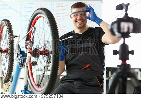 Smiling Male Blogger In Special Clothes Holding Spanner While Demonstrating Bike Repair On Camera