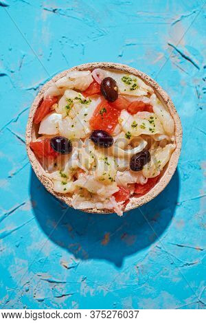 high angle view of a plate with esqueixada de bacalla, a cold dish made with codfish, tomato, onion and black olives, and dressed with olive oil, typical of Catalonia, Spain, on a blue rustic surface