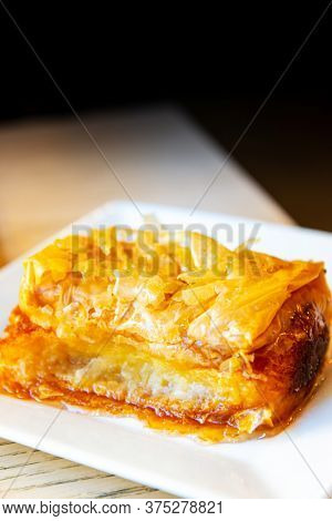 Delicious Greek sweet pastry named Galaktoboureko, made of semolina custard in filo, served with honey in white plate.