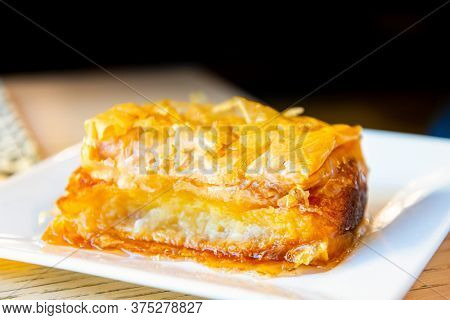 Delicious Greek sweet pastry named Galaktoboureko, made of semolina custard in filo, served with honey in white plate.