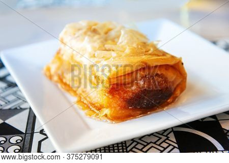 Delicious Greek sweet pastry named Galaktoboureko, made of semolina custard in filo, served with honey in white plate.