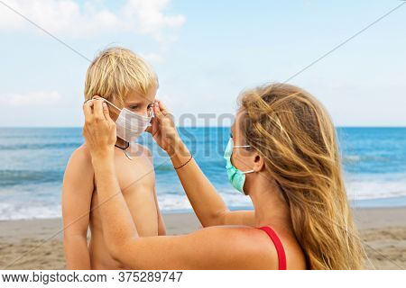 Mother Put Medical Mask On Child On Sea Beach. New Rules To Wear Cloth Face Covering At Public Place