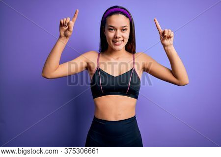 Young beautiful sporty girl doing sport wearing sportswear over isolated purple background smiling amazed and surprised and pointing up with fingers and raised arms.