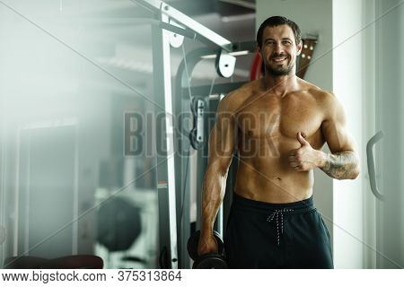 Fitness in gym, sport and healthy lifestyle concept. Handsome athletic man with naked torso making exercises. Bodybuilder male model standing and showing thumb up.