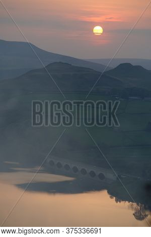 Calm Ladybower Reservoir Water Beneath An Arched Bridge Reflects The Orange Sunset From Above The Ta
